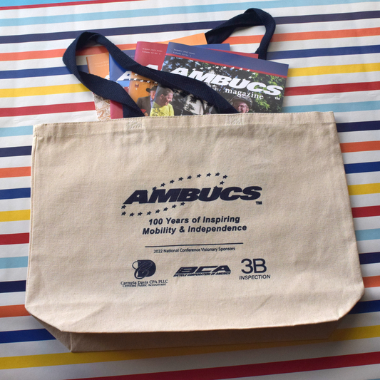 Canvas tote bag with blue handles. The AMBUCS logo and the words 100 years of Inspiring Mobility and independence .is printed is blue